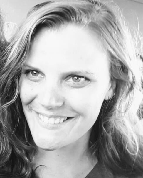 Black and white photo, showing the face of a white woman with shoulder length hair, smiling and looking to the left of the camera